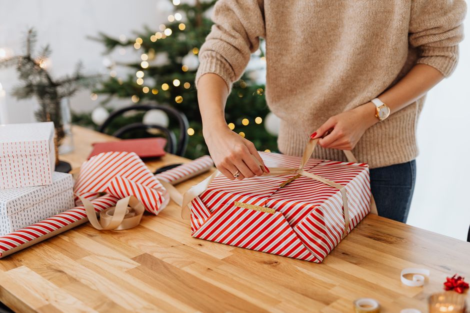 Elle kraft kağıdı ve kurdeleyle hediye paketleyen kişi